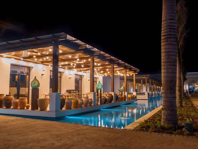 Oświetlony salon z basenem i miejscami do siedzenia nocą, otoczony palmami.