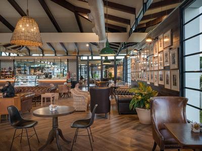 Nowoczesna kawiarnia z drewnianą podłogą, czarnymi krzesłami i dużymi oknami z widokiem na zieleń.