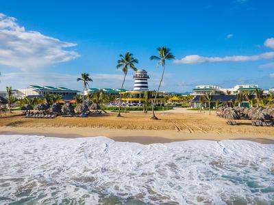 Strand mit goldfarbenem Sand, Palmen, Sonnenschirmen und blauem Himmel mit Wolken.