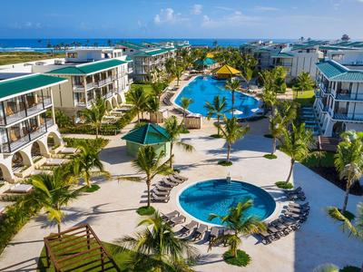 Vogelperspektive eines Resorts mit drei Pools, umgeben von Palmen und Gebäuden nahe der Küste.