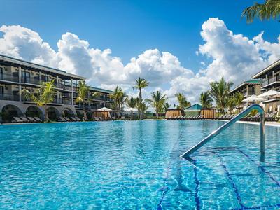 Großer Hotelpool mit klar blauem Wasser, umgeben von mehrstöckigen Gebäuden und Palmen.