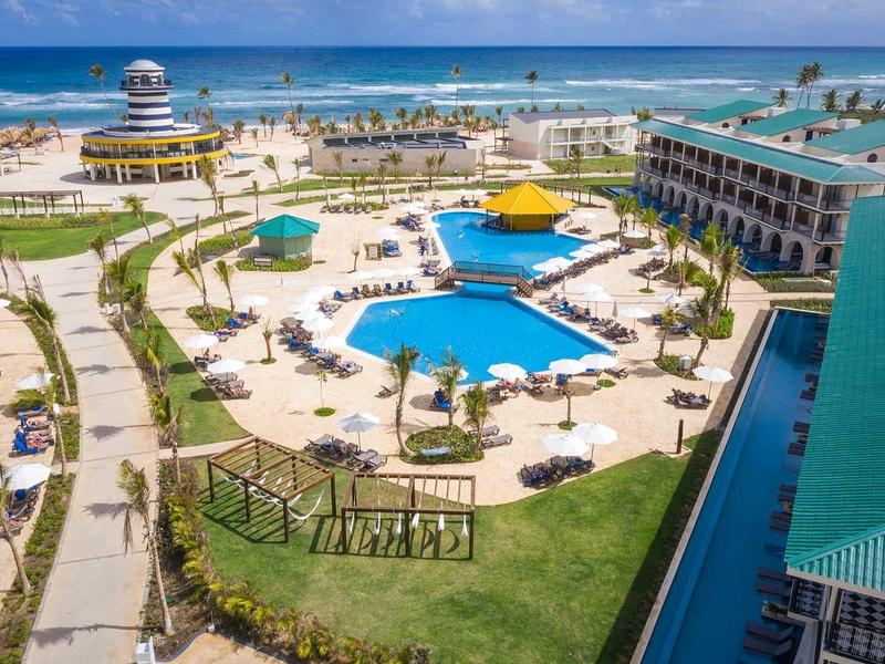 Blick auf einen großen Pool mit Sonnenschirmen, Liegestühlen und einem Hotel am Meer.