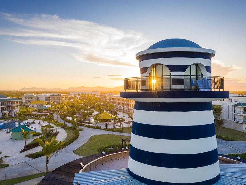 Blaue und weiße Leuchtturmstruktur bei Sonnenuntergang mit modernem Wohngebiet im Hintergrund.