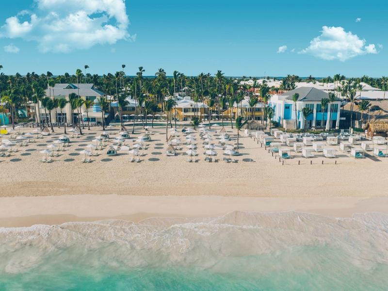 Strand mit Reihen von Liegestühlen, Palmen im Hintergrund und blauem Himmel mit Wolken.
