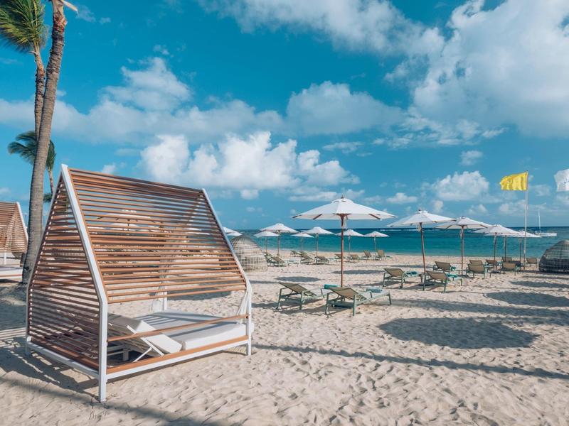 Strand mit Sand, modernen Holzzelten, Palmen und blauem Himmel mit Wolken.