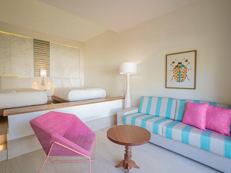 Moderner Wohnzimmerbereich mit blau-weiß gestreiftem Sofa, pinkem Sessel und rundem Holztisch.