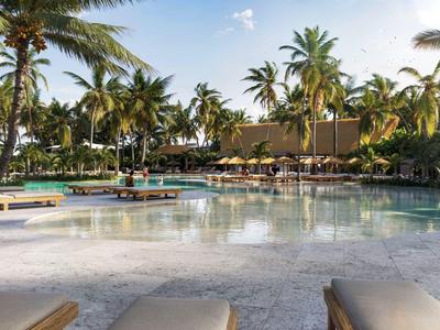 Piscine avec chaises longues et palmiers dans une station tropicale au coucher du soleil.