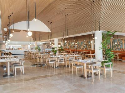 Large modern hotel restaurant area with wooden ceiling and many tables and chairs.