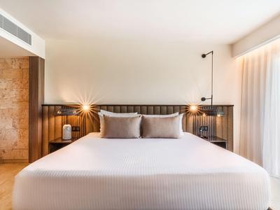 Modern bedroom with large bed, bright walls, and natural light from window.
