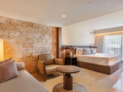 Bright hotel room with stone accent wall, two beds, and seating area with table.