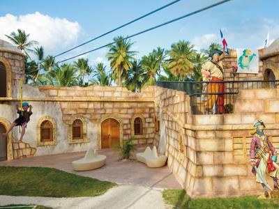 Barevný zábavní park s kamennými zdmi ve tvaru pevnosti a tropickými palmami v pozadí.