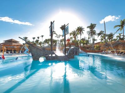Swimming pool with pirate ship playground and palm trees under sunny sky at a holiday resort