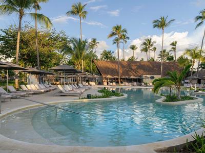 Swimming pool with sun loungers and palm trees at tropical resort under blue sky.