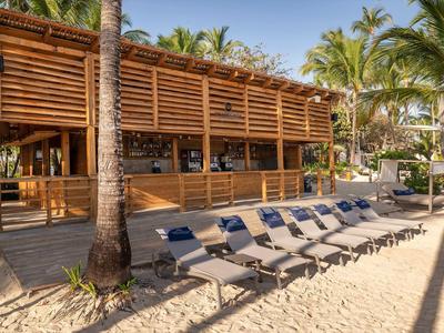 Beach bar with wooden structure and lounge chairs on sand under palm trees
