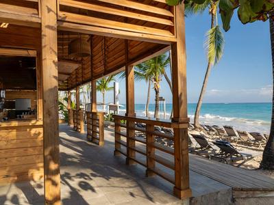 Wooden terrace overlooking the beach, palm trees, and lounge chairs by the sea.