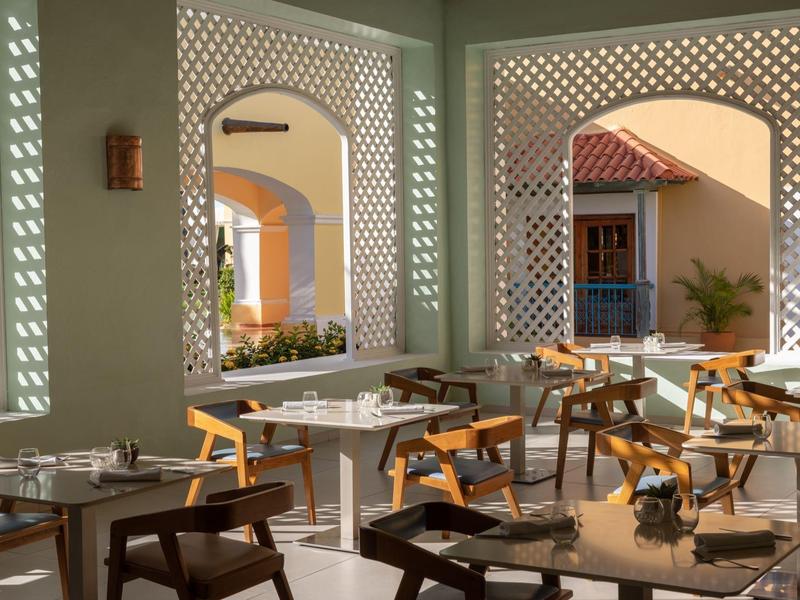 Jasně osvětlený hotelový restaurace s stolky a židlemi v otevřeném, architektonicky navrženém prostoru.