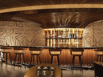 Moderní hotelový bar s dřevěnými barovými židličkami a abstraktními vzory na stěnách.