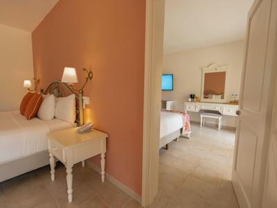 Przytulny pokój hotelowy z białymi meblami i małym stolikiem nocnym przy łóżku.