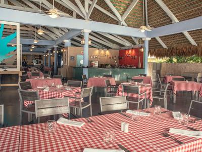 Offenes Restaurant mit rot-weiß karierten Tischdecken, Holzstühlen und sichtbaren Deckenbalken.