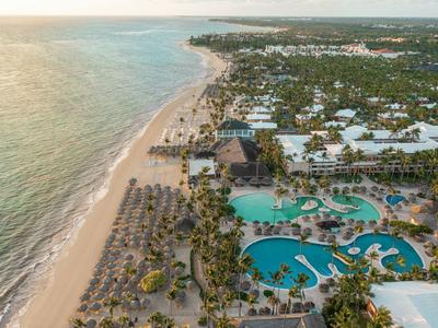 Luftaufnahme eines tropischen Strandes mit Palmen, türkisfarbenem Pool und Hotelanlage am Meer.