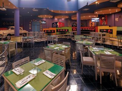 Restaurant mit blau-lila Wänden, Holzstühlen und Tischen, grüne Tischsets, moderne Beleuchtung.