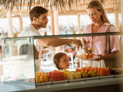 Familie wählt frisch geschnittenes Obst in einem Marktstand mit Strohdach aus.