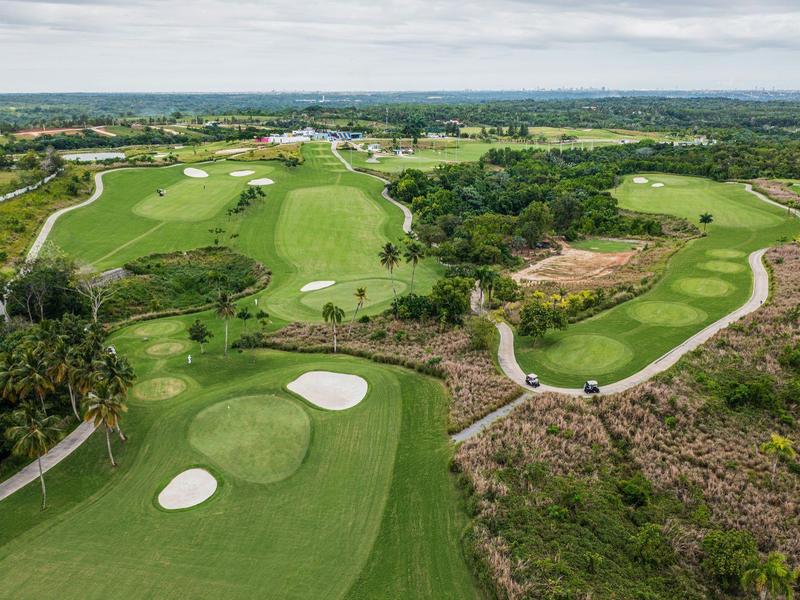 Widok z lotu ptaka na zadbany golfowy pole z zielenią i bunkrami na tle szerokiego krajobrazu.