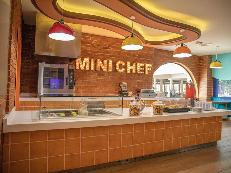 Nowoczesna kuchnia hotelowa z napisem „MINI CHEF” i ladą na pierwszym planie.