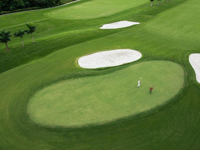 Dwóch golfistów gra na zadbanym, zielonym polu golfowym z bunkrami z piasku.