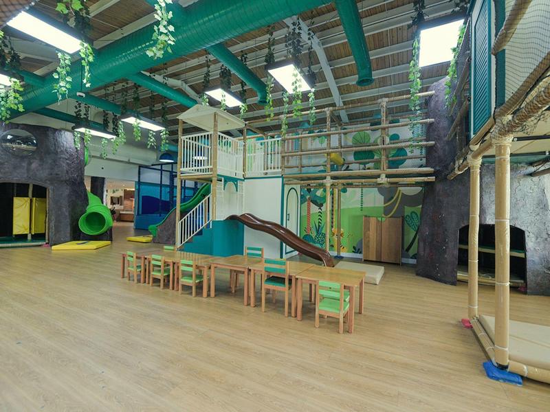 Widok wnętrza dużego placu zabaw krytego z konstrukcjami do wspinaczki, zjeżdżalniami i miejscami do siedzenia.