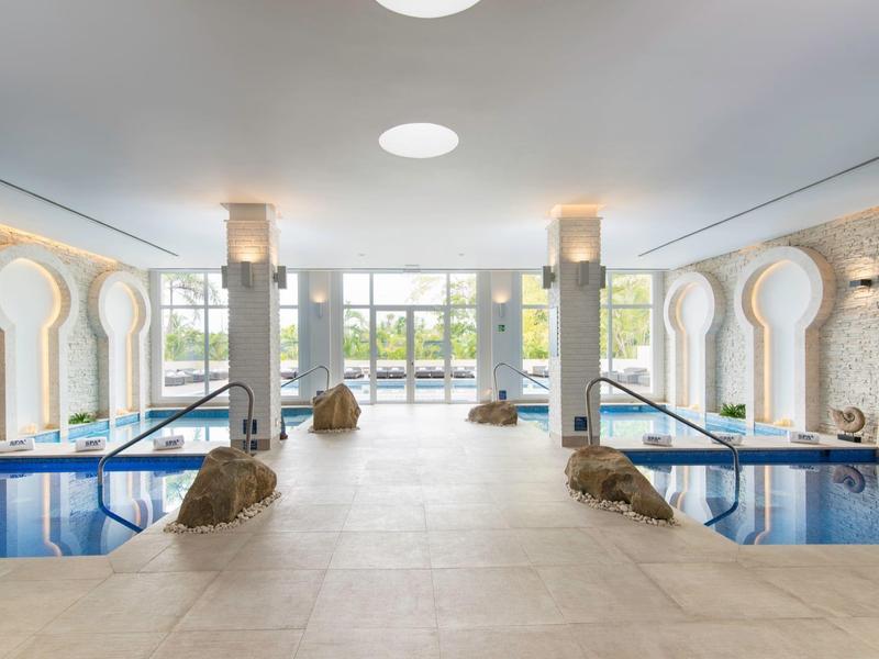 Nowoczesny basen kryty z dużymi oknami i śródziemnomorskimi łukami w jasnym otoczeniu.