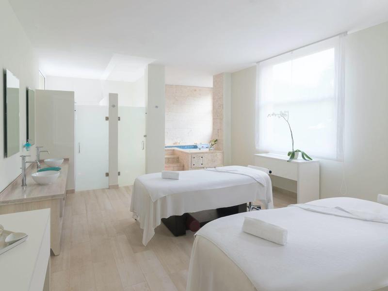 Bright treatment room with two massage tables and large windows for natural lighting.