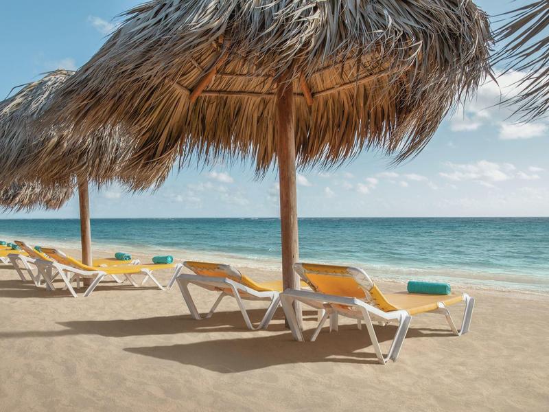 Empty lounge chairs under straw roofs on sandy beach overlooking the sea.