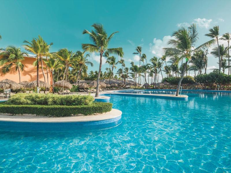 Large pool with palm trees and blue sky in tropical vacation resort.