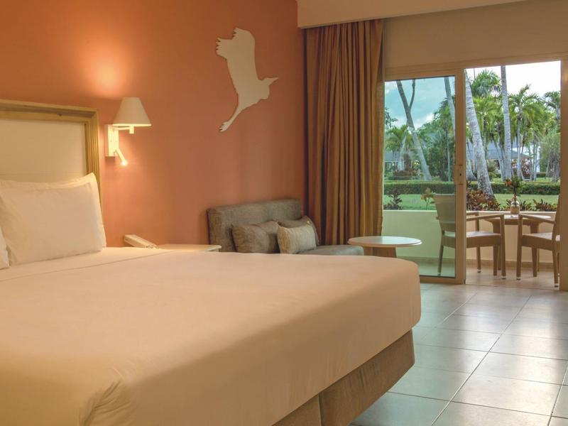 A cozy hotel room with a large bed, chair, and view of a terrace with garden.