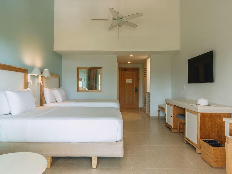 Modern hotel room with two beds, ceiling fan, and flat-screen TV on the wall.