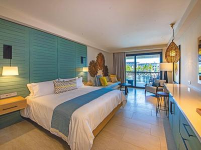 Helles Hotelzimmer mit großem Bett, blauen Wandpaneelen und Zugang zu Balkon mit Meerblick.