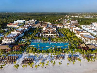 Blick auf ein großes Resort mit Pool, Palmen und Strand an der Küste bei klarem Himmel.