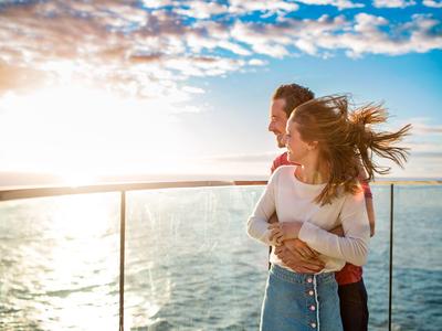 Paar steht auf Balkon mit Meerblick bei Sonnenuntergang.