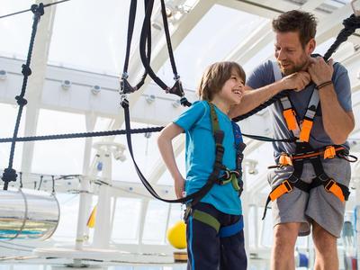 Vater und Sohn beim Klettern in einer Halle mit Sicherheitsgurten und Helmen.