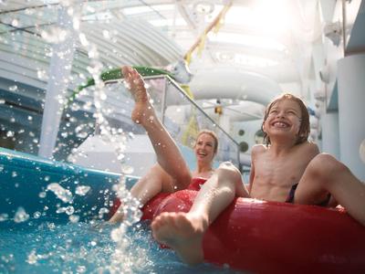 Zwei Kinder genießen einen Wasserpark auf einem roten Reifen mit spritzendem Wasser.