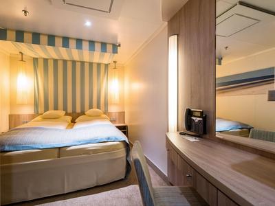 Kompaktes Hotelzimmer mit Doppelbett, Spiegel, Schreibtisch und sanfter Beleuchtung.