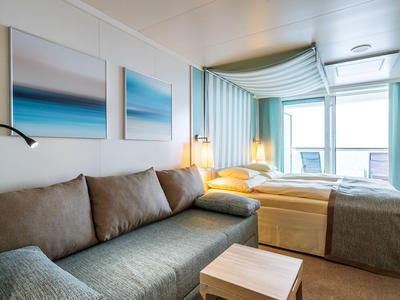 Helles Hotelzimmer mit Sofa, Bett, modernen Bildern und viel Tageslicht.