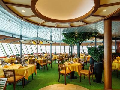 Geräumiges Restaurant mit gelb gedeckten Tischen, Holzstühlen und großen Fenstern