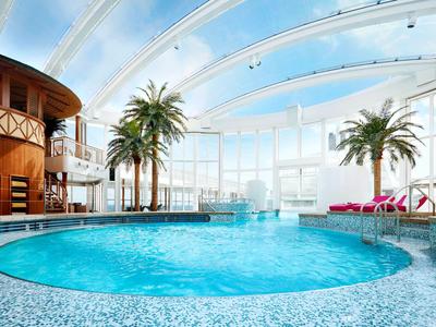 Moderner Innenpool mit runder Form, großen Glasfenstern und Palmen im Hotel.