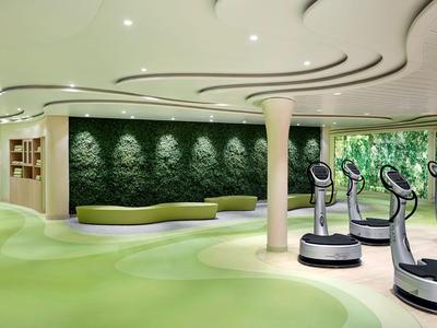 Moderner Fitnessraum mit grüner Wandgestaltung und Vibrationsplatten im Hotel.