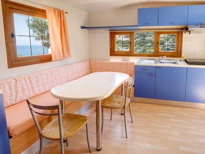 Jasna kuchnia z niebieskimi szafkami, drewnianą podłogą, stołem, krzesłami i oknem z widokiem na morze.