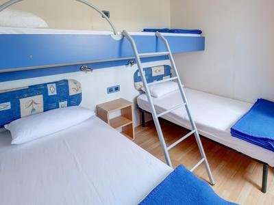 Mała sypialnia z dwoma łóżkami piętrowymi, białe ściany i niebieskie koce.