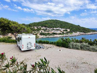 Wohnmobil auf einem Parkplatz mit Blick auf das Meer und ein Dorf auf einem Hügel