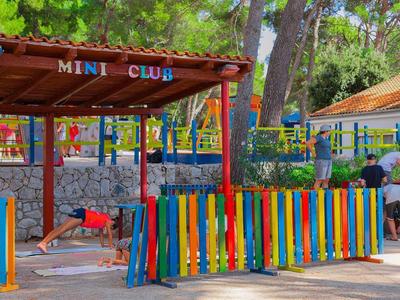 Kolorowy plac zabaw dla dzieci z budką mini klubu i kilkorgiem dzieci na zewnątrz.